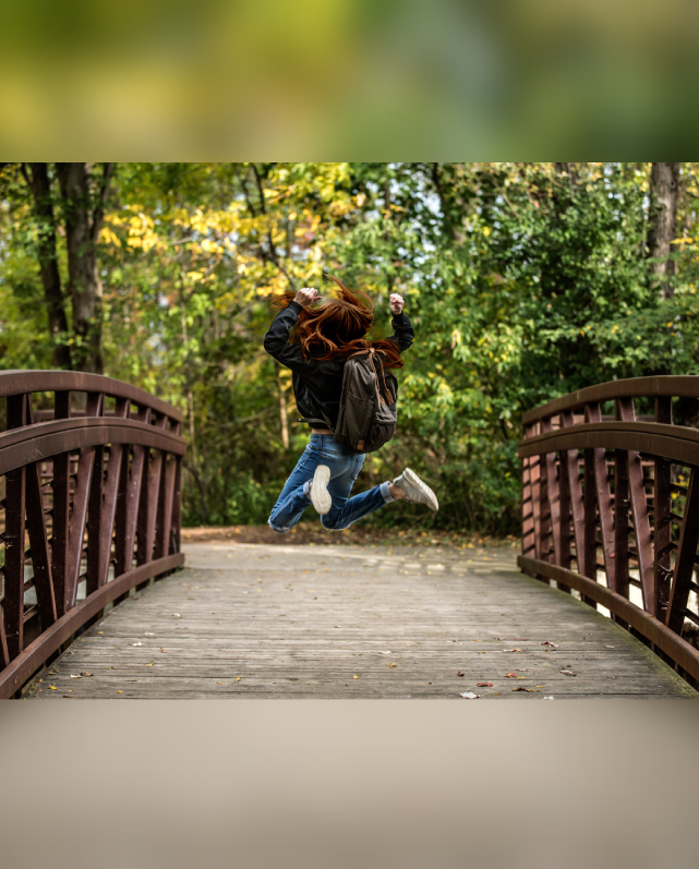 Child jumping joyfully on a wooden bridge in autumn woods